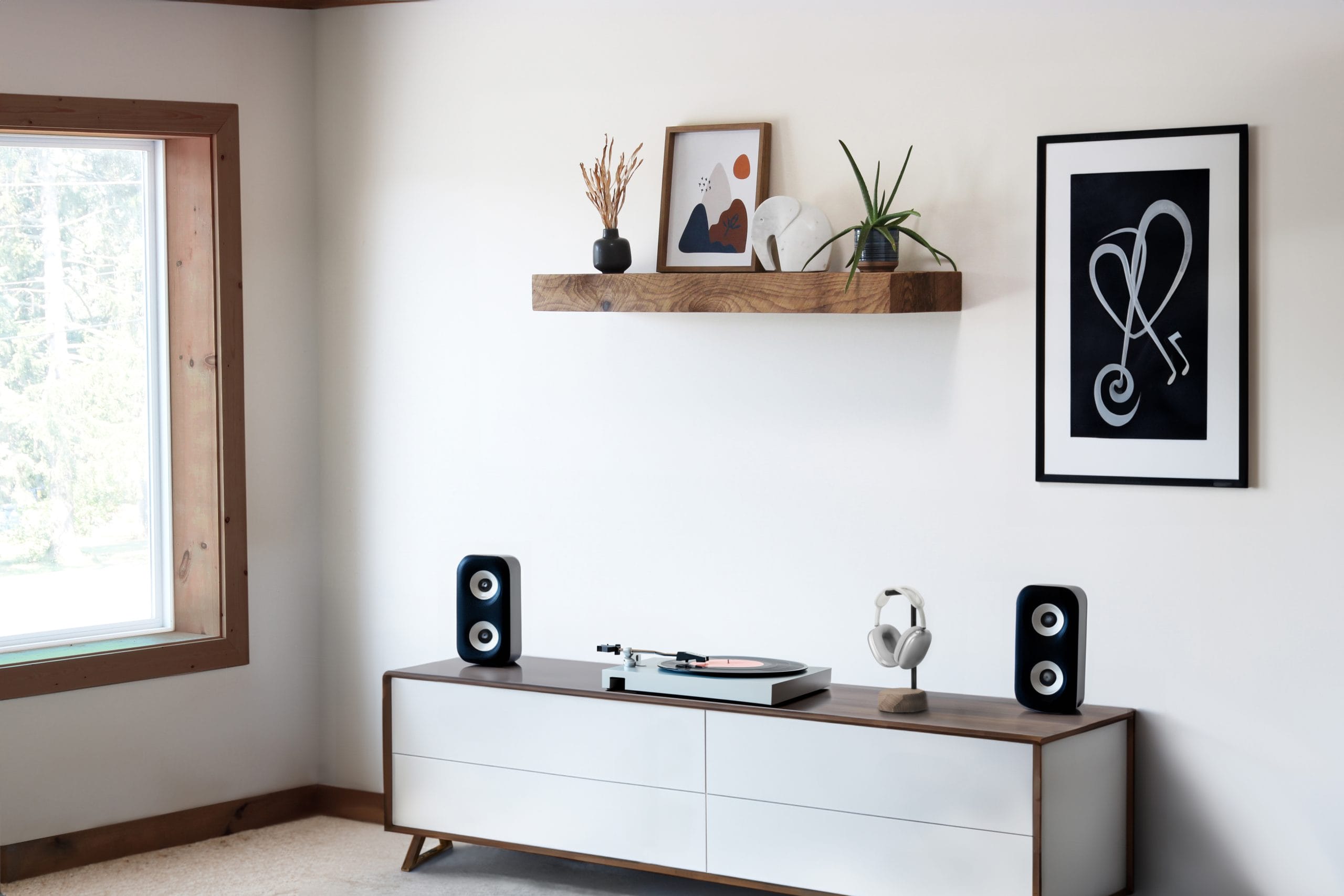 Minimalistic room showcasing a floating reclaimed wood shelf adorned with modern decor items, against a light wall with a framed artwork and a view to the outdoors.